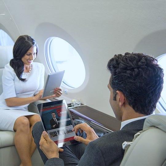在一架私人飞机上，一男一女面对面坐在一起，用平板电脑看机上娱乐节目