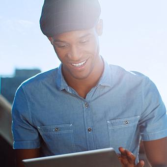 一名身穿蓝色系扣衬衫、头戴平顶帽的男子对着平板电脑微笑