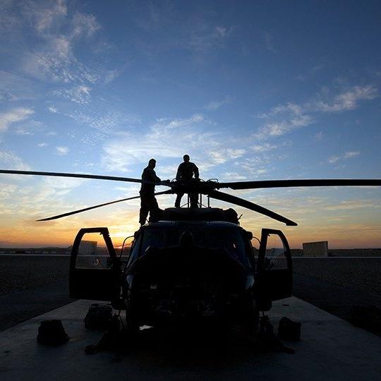 日落时分，两名战士在直升机顶上检查旋翼