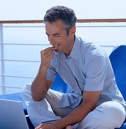 Man sitting on the deck of a passenger boat using a laptop with satellite internet for boats