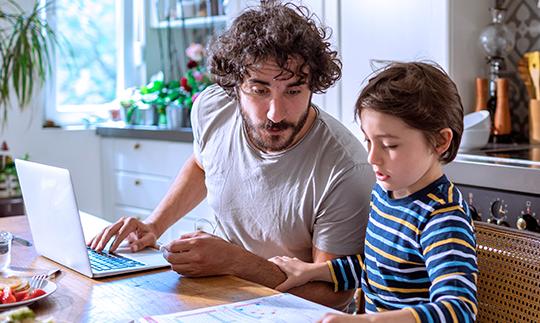 在Viasat的卫星互联网和联邦通信委员会的平价连接计划的帮助下，爸爸和儿子在笔记本电脑上做作业.